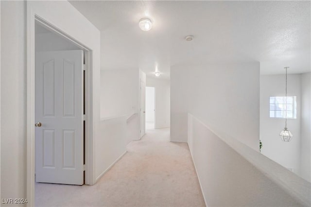 hall with a textured ceiling and light colored carpet