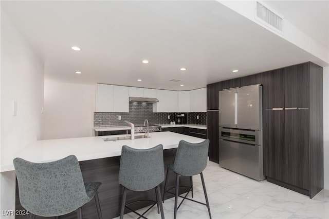 kitchen with sink, a kitchen breakfast bar, stainless steel fridge, decorative backsplash, and white cabinets