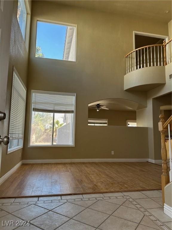 unfurnished living room with ceiling fan, light hardwood / wood-style flooring, and a high ceiling