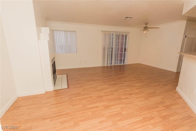 unfurnished living room featuring a tile fireplace, ceiling fan, crown molding, and light wood-type flooring