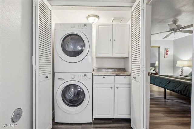 laundry area with stacked washer / drying machine, ceiling fan, cabinets, and dark wood-type flooring