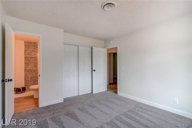 unfurnished bedroom with ensuite bath, a closet, carpet floors, and a textured ceiling