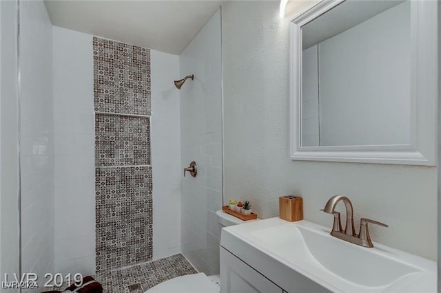 bathroom with a tile shower, vanity, and toilet