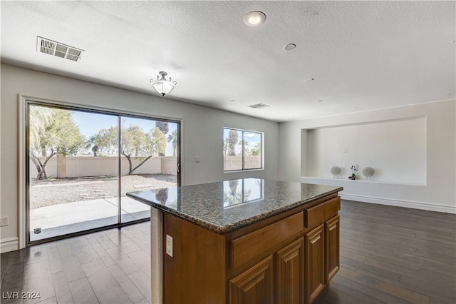 kitchen featuring dark stone countertops, dark wood-type flooring, a textured ceiling, and a kitchen island