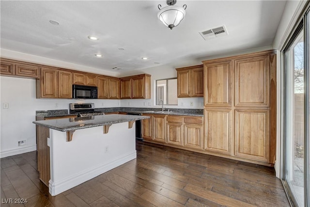 kitchen featuring dark wood-type flooring, stainless steel range oven, sink, a center island, and dark stone countertops