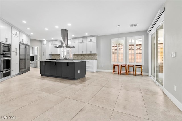 kitchen featuring white cabinetry, tasteful backsplash, ventilation hood, built in appliances, and an island with sink