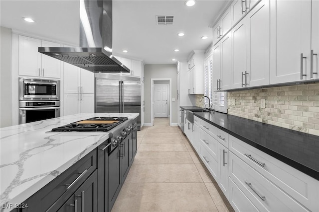 kitchen with dark stone counters, white cabinets, built in appliances, light tile patterned floors, and extractor fan