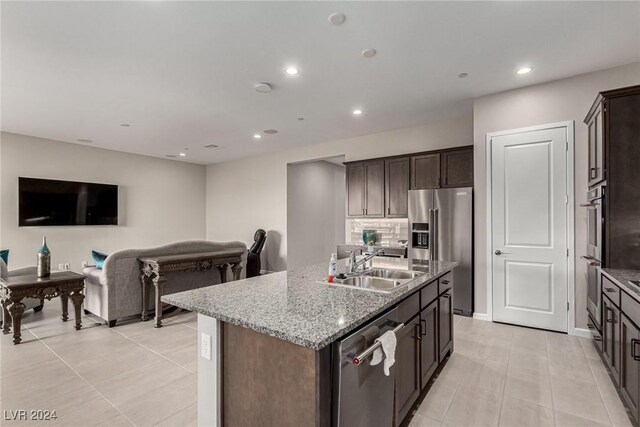 kitchen featuring appliances with stainless steel finishes, light stone counters, dark brown cabinetry, sink, and an island with sink