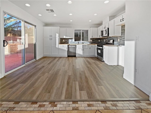 kitchen featuring backsplash, stainless steel appliances, white cabinetry, and light hardwood / wood-style flooring