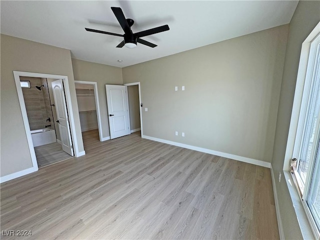 unfurnished bedroom with a walk in closet, ceiling fan, ensuite bath, and light wood-type flooring