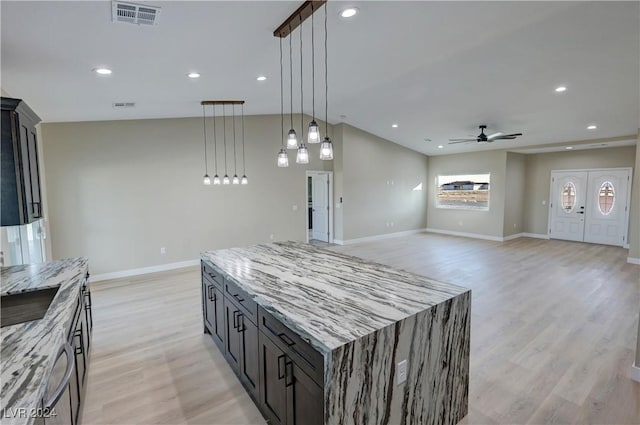 kitchen with hanging light fixtures, light hardwood / wood-style flooring, ceiling fan, a kitchen island, and light stone counters