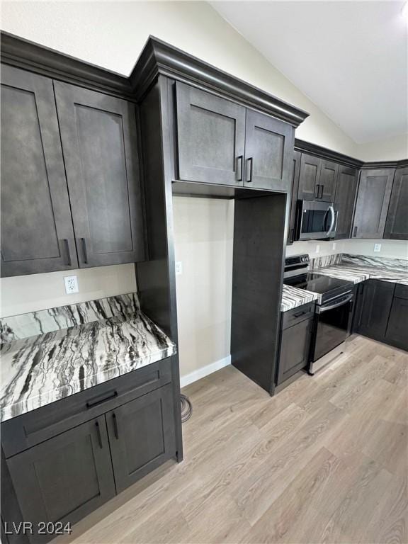 kitchen featuring light stone counters, stainless steel appliances, vaulted ceiling, and light wood-type flooring