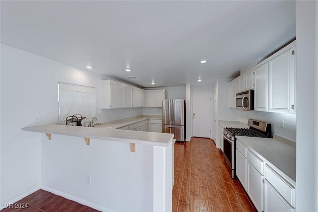 kitchen featuring kitchen peninsula, hardwood / wood-style floors, stainless steel appliances, and white cabinetry