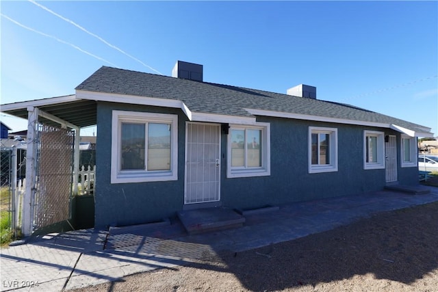 view of front of property with a chimney, stucco siding, a shingled roof, a patio area, and fence