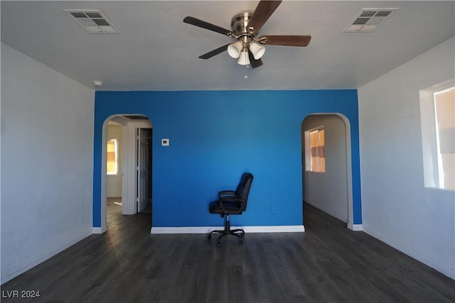 unfurnished office featuring arched walkways, dark wood finished floors, visible vents, and baseboards