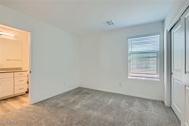 unfurnished bedroom with light colored carpet and connected bathroom