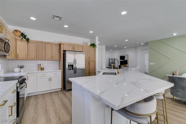 kitchen with light stone countertops, sink, stainless steel appliances, light hardwood / wood-style flooring, and a large island with sink