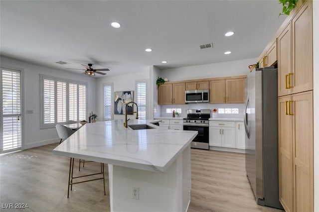 kitchen with a kitchen island with sink, sink, light hardwood / wood-style flooring, light stone countertops, and stainless steel appliances