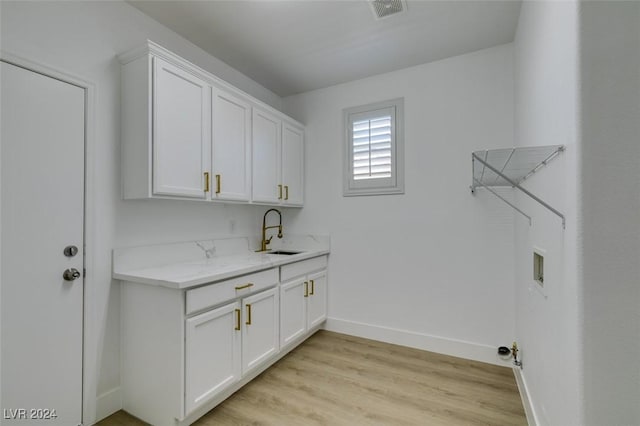 clothes washing area featuring cabinets, sink, washer hookup, and light wood-type flooring