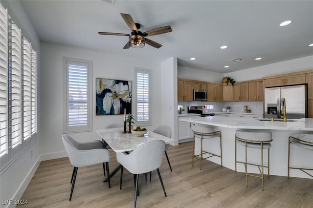 kitchen with a breakfast bar, appliances with stainless steel finishes, light hardwood / wood-style floors, and a center island with sink