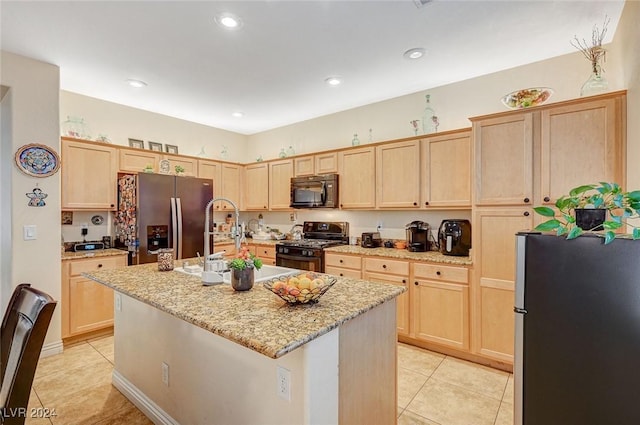 kitchen featuring light stone countertops, an island with sink, light brown cabinetry, light tile patterned flooring, and black appliances