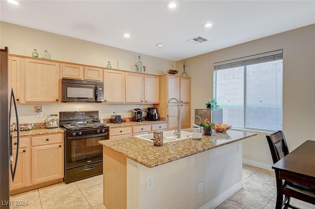 kitchen featuring light stone countertops, light brown cabinetry, black appliances, light tile patterned floors, and a center island with sink