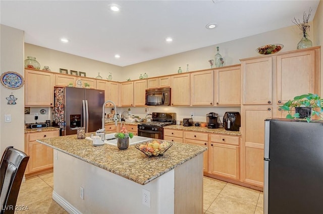 kitchen with light stone countertops, an island with sink, light brown cabinetry, light tile patterned floors, and black appliances