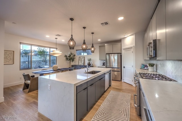 kitchen with sink, stainless steel appliances, pendant lighting, gray cabinets, and a center island with sink