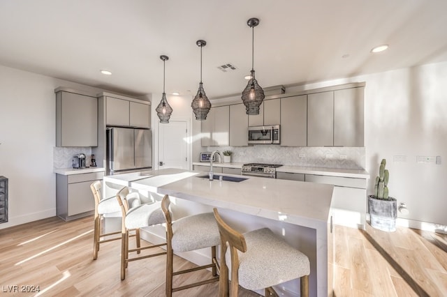 kitchen featuring gray cabinetry, stainless steel appliances, sink, pendant lighting, and light hardwood / wood-style flooring