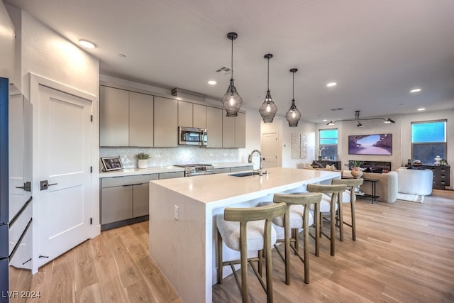 kitchen with light wood-type flooring, gray cabinetry, stainless steel appliances, a kitchen island with sink, and sink