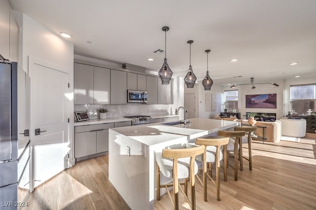 kitchen with gray cabinetry, sink, light wood-type flooring, appliances with stainless steel finishes, and decorative light fixtures