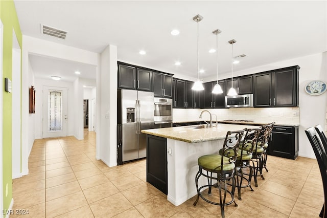 kitchen featuring pendant lighting, sink, light stone countertops, an island with sink, and appliances with stainless steel finishes