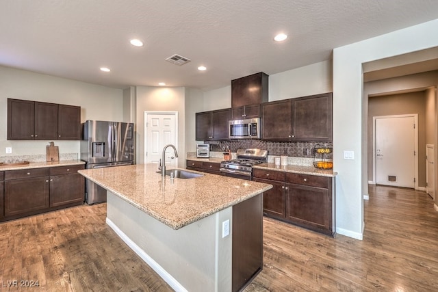 kitchen featuring sink, light hardwood / wood-style flooring, an island with sink, appliances with stainless steel finishes, and dark brown cabinets