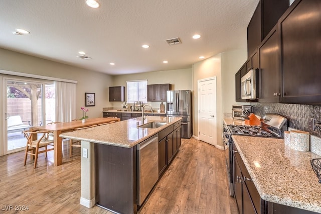 kitchen with a kitchen island with sink, sink, light wood-type flooring, and appliances with stainless steel finishes