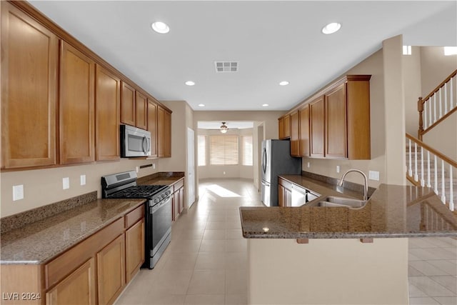 kitchen with a breakfast bar, stainless steel appliances, dark stone counters, and sink