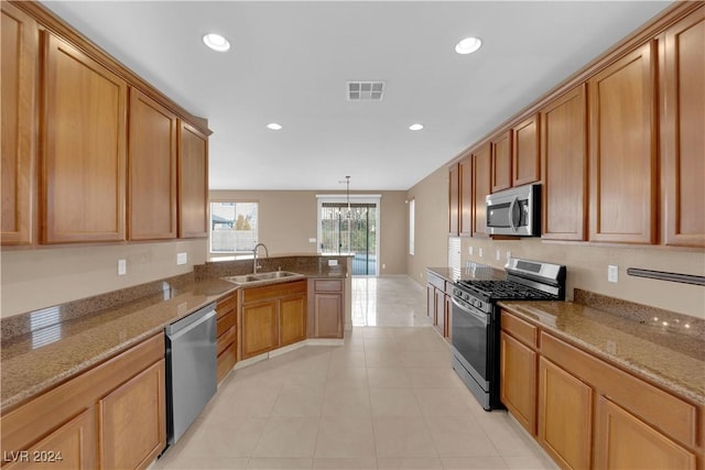 kitchen with appliances with stainless steel finishes, sink, pendant lighting, stone countertops, and an inviting chandelier