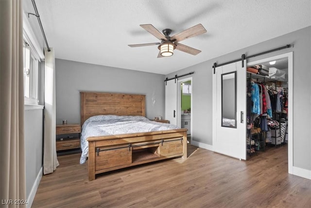 bedroom with ceiling fan, a barn door, hardwood / wood-style floors, a textured ceiling, and a closet