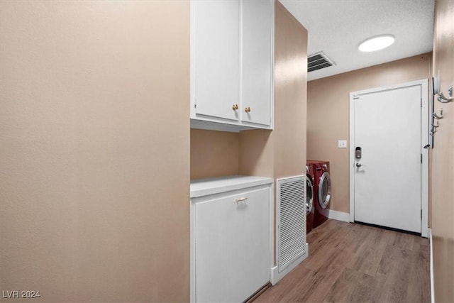 laundry room with cabinets, a textured ceiling, washing machine and dryer, and light hardwood / wood-style flooring