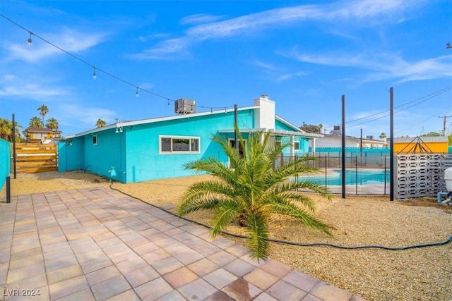 rear view of house with cooling unit, a fenced in pool, and a patio