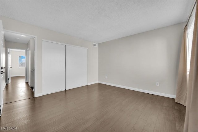 unfurnished bedroom featuring dark hardwood / wood-style flooring, a textured ceiling, and a closet