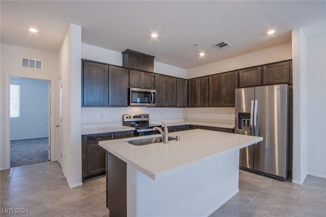 kitchen with dark brown cabinetry, stainless steel appliances, sink, light tile patterned floors, and an island with sink