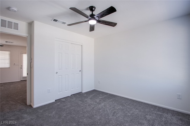 unfurnished bedroom with ceiling fan, a closet, and dark colored carpet