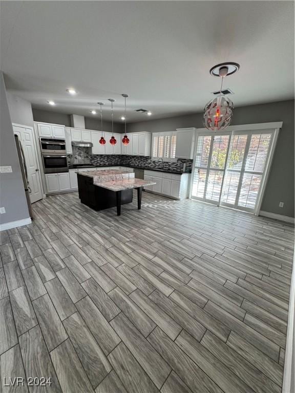 kitchen featuring white cabinets, light hardwood / wood-style flooring, appliances with stainless steel finishes, decorative light fixtures, and a kitchen island