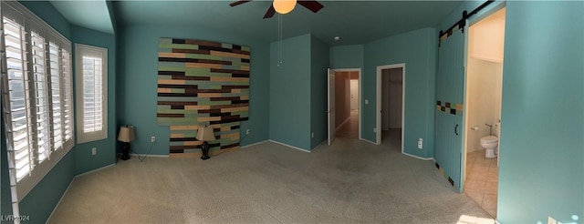 carpeted spare room featuring a barn door and ceiling fan