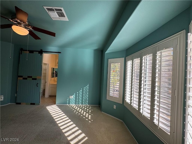 spare room with light carpet, a barn door, and ceiling fan