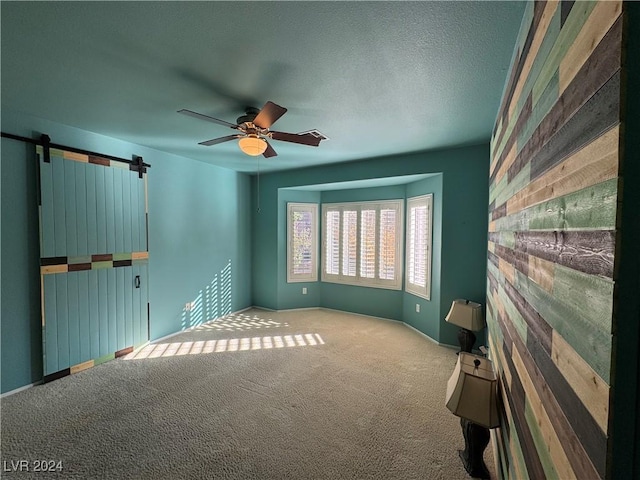 carpeted spare room featuring a barn door, ceiling fan, and a textured ceiling