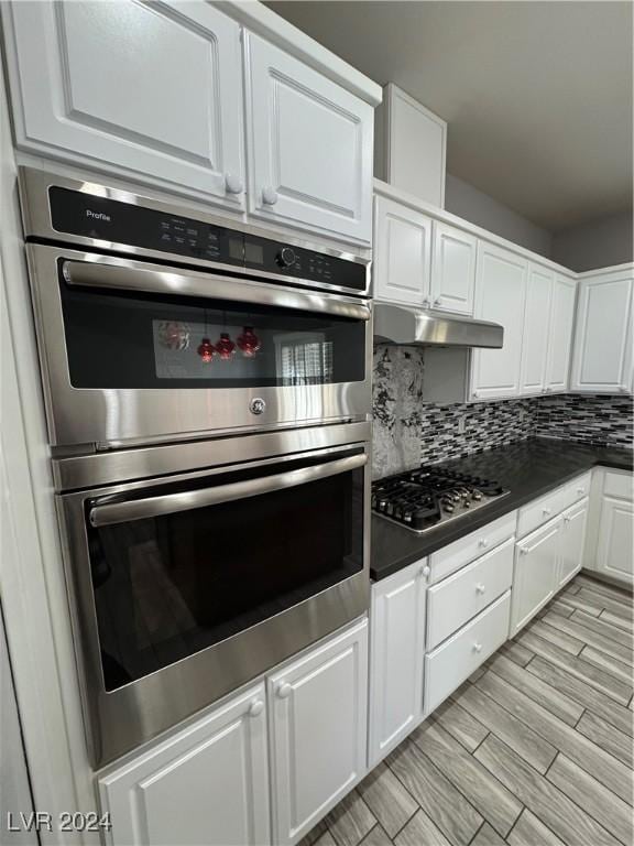 kitchen with decorative backsplash, white cabinetry, light wood-type flooring, and appliances with stainless steel finishes