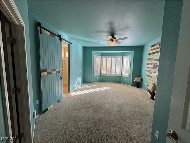 carpeted empty room featuring a barn door and ceiling fan