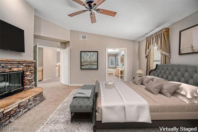 bedroom with ensuite bathroom, light colored carpet, ceiling fan, a stone fireplace, and lofted ceiling