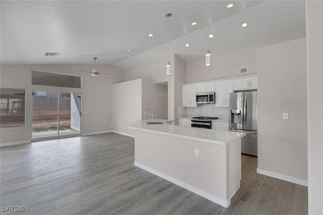 kitchen with a kitchen island with sink, white cabinets, appliances with stainless steel finishes, decorative light fixtures, and light hardwood / wood-style floors